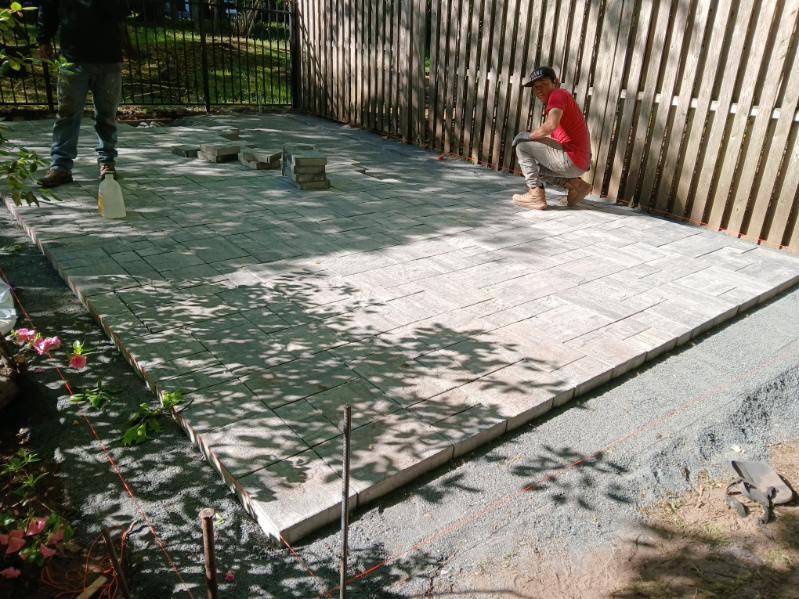Paver patio installation in progress beneath mature trees